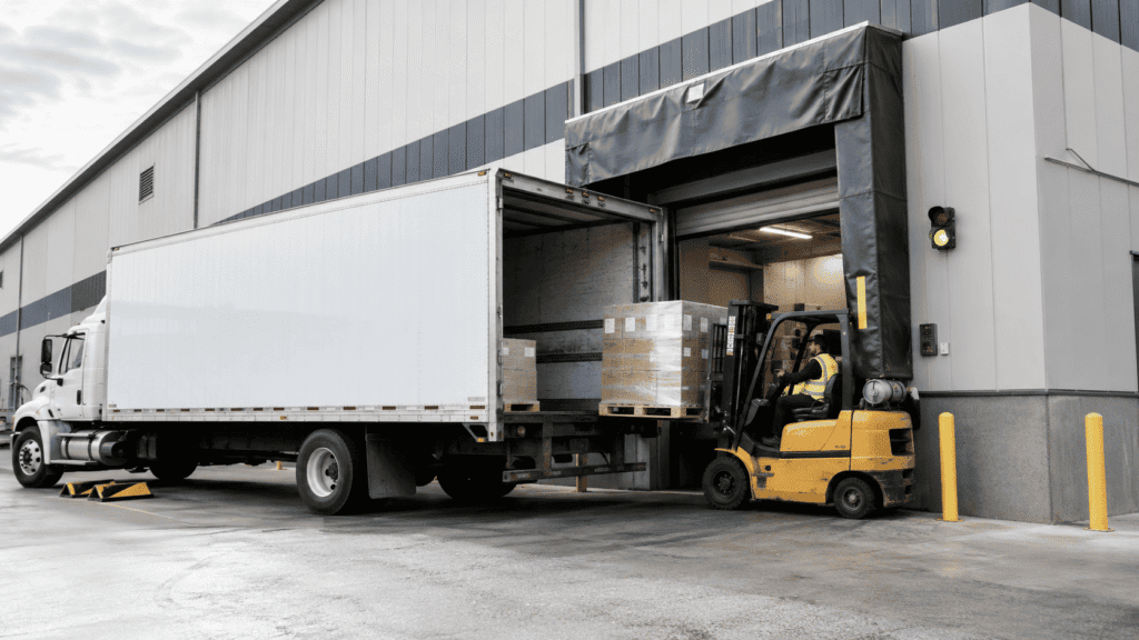 Forklift loading pallets into a truck at a warehouse loading dock door with dock shelter and safety equipment