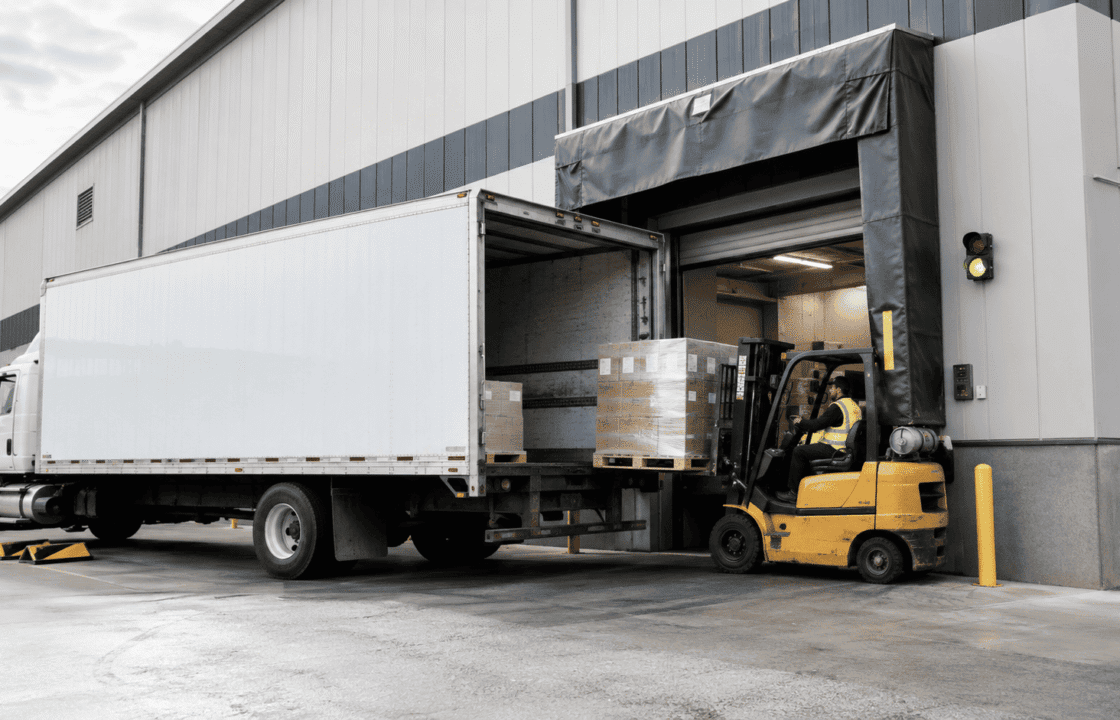 Forklift loading pallets into a truck at a warehouse loading dock door with dock shelter and safety equipment