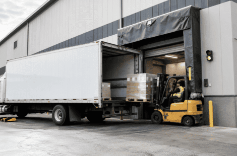 Forklift loading pallets into a truck at a warehouse loading dock door with dock shelter and safety equipment