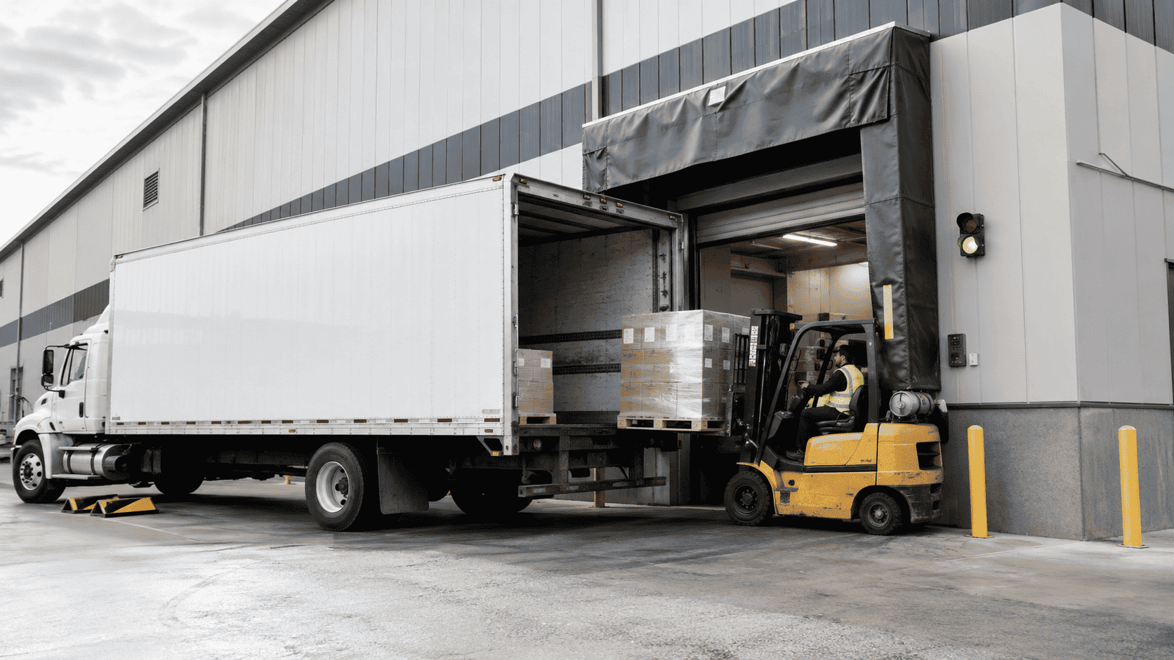 Forklift loading pallets into a truck at a warehouse loading dock door with dock shelter and safety equipment